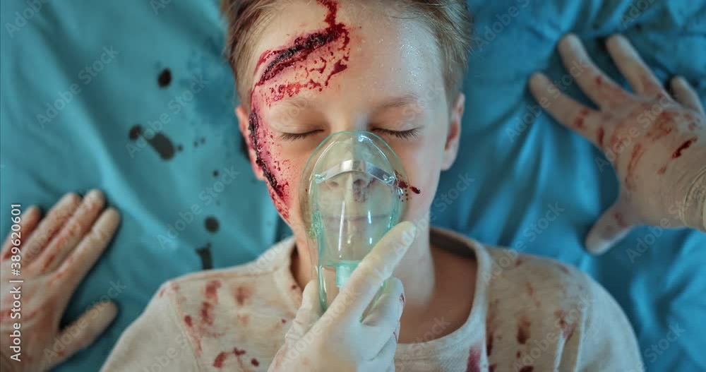 Paramedics doing cardiac massage and putting oxygen inhalation mask to little boy. Close up of unconscious child with head unjuries lying on medical transportation stretcher