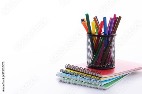 collection of colorful felt-tip pens in cup with notebooks on light background, close view. High quality photo