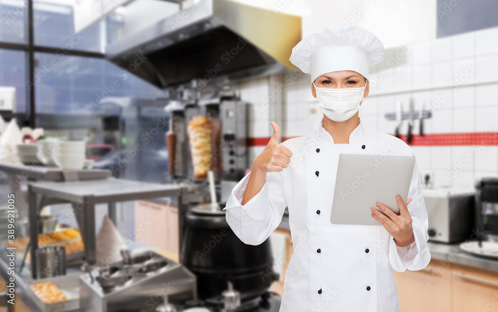 cooking, culinary and health concept - female chef in toque wearing face medical mask for protection from virus disease with tablet pc computer showing thumbs up over kebab shop kitchen background