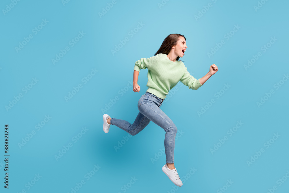 Full length body size side profile photo of cheerful female student running fast hurrying up jumping high laughing isolated on bright blue color background