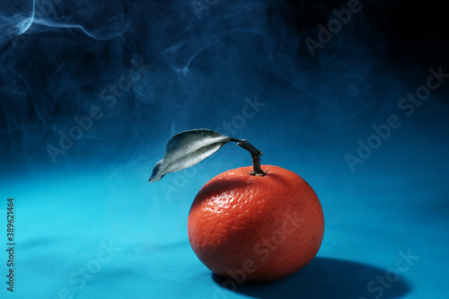 One fresh tangerine with leaves lies on a blue wooden table. Mysty photography with empty space for text photo