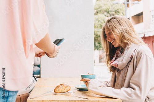Girl's hands taking a picture of a breakfast while her friend is having a coffee and smiling.