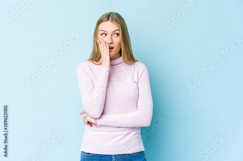 Young blonde woman isolated on blue background is saying a secret hot braking news and looking aside © Asier