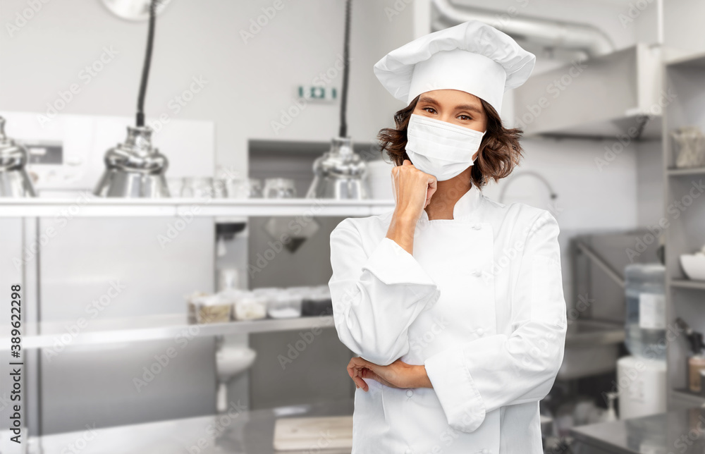cooking, culinary and health concept - female chef in toque wearing face protective medical mask for protection from virus disease over restaurant kitchen background cooking, culinary and health concept - female chef in toque wearing face protective medical mask for protection from virus disease over restaurant kitchen background