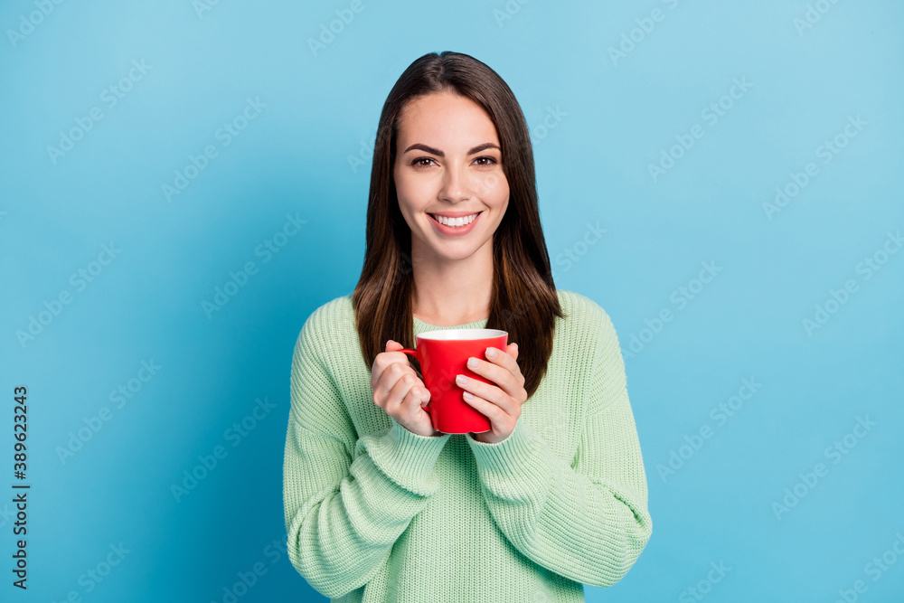Photo portrait of brunette girl keeping hot cup of tea smiling wearing green jumper isolated on vibrant blue color background Photo portrait of brunette girl keeping hot cup of tea smiling wearing green jumper isolated on vibrant blue color background