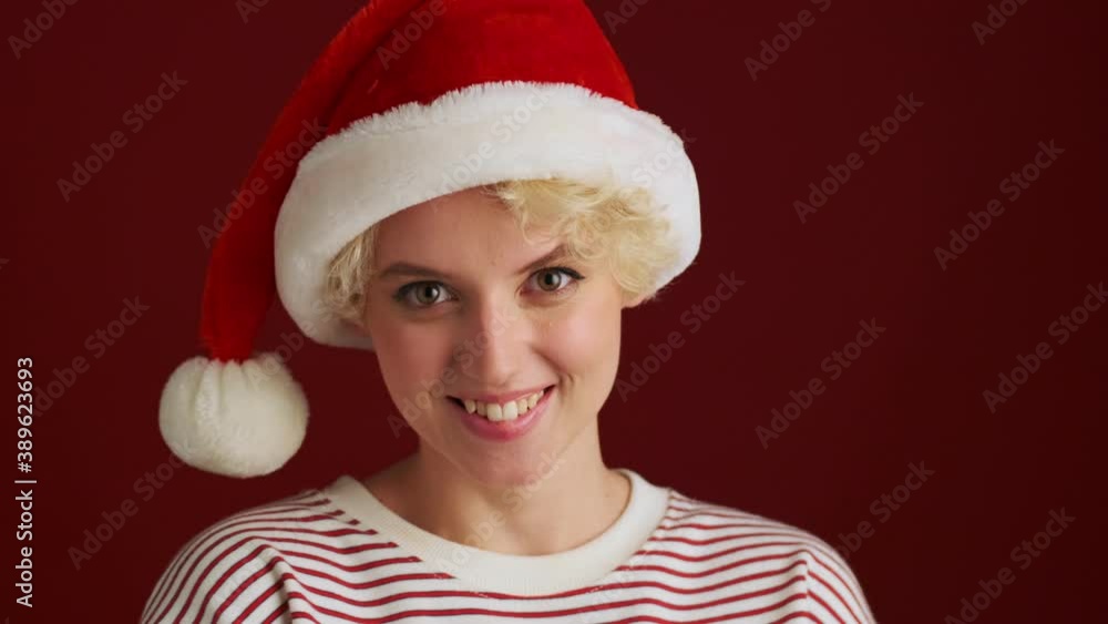 Young cheerful happy girl looking at the camera in christmas santa hat isolated over red wall background Young cheerful happy girl looking at the camera in christmas santa hat isolated over red wall background