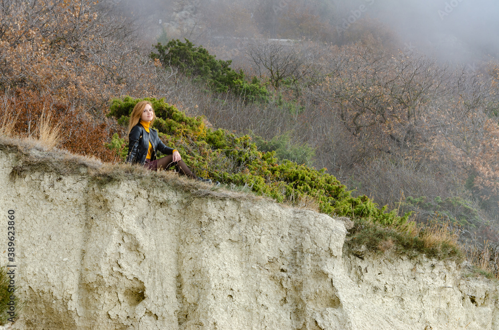 Obraz premium A girl sits on a hillock in the mountains and enjoys a wonderful view