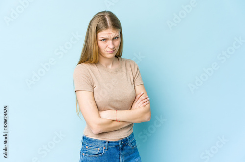 Young blonde woman isolated on blue background frowning face in displeasure, keeps arms folded. © Asier