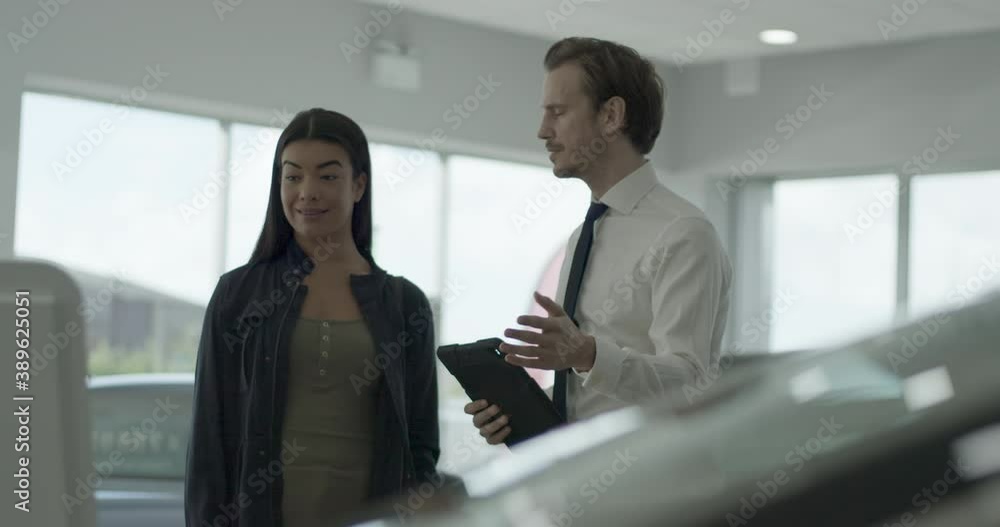 Car sales person talking to customer in car dealership showroom, looking at digital tablet Car sales person talking to customer in car dealership showroom, looking at digital tablet