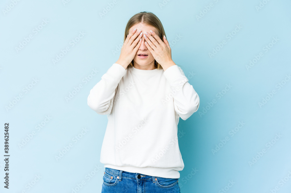 Young blonde woman isolated on blue background afraid covering eyes with hands. Young blonde woman isolated on blue background afraid covering eyes with hands.