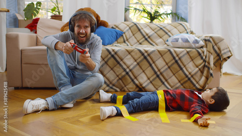 Photography Father in headphones playing video game with console and disobedient son tied wi
