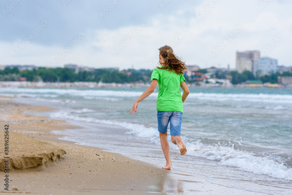 A girl happily runs along the sea coast, view from the back