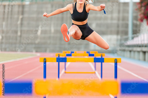 Fit female teenager athlete hurdler running jumping over hurdles photo