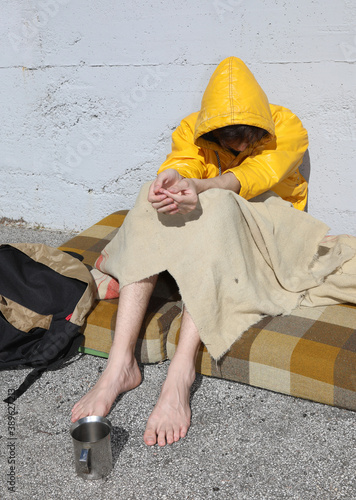 poor barefoot homeless man in a yellow hood asks for charity fro photo