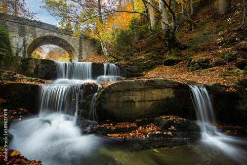 Fototapeta Naklejka Na Ścianę i Meble -  Autumn waterfalls near Sitovo, Plovdiv, Bulgaria. Beautiful cascades of water with fallen yellow leaves under the bridge. Sitovski waterfall