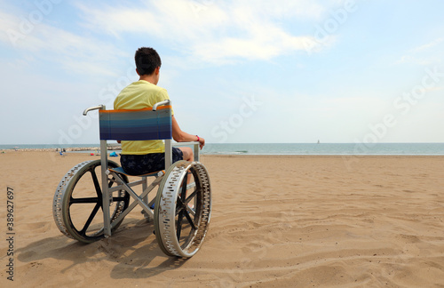 young disabled boy in the wheelchair on the sandy beach by the s