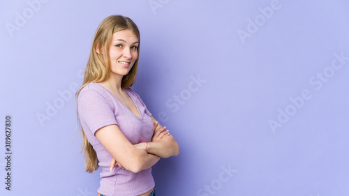 Young blonde woman isolated on purple background who feels confident, crossing arms with determination.
