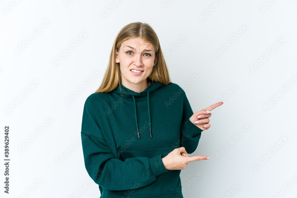 Young blonde woman isolated on white background shocked pointing with index fingers to a copy space. Young blonde woman isolated on white background shocked pointing with index fingers to a copy space.