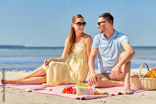 leisure, relationships and people concept - happy couple in sunglasses having picnic on summer beach