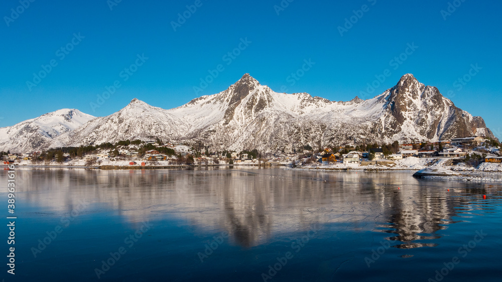 Beautiful winter landscape with lake and steep mountains near Svolvaer on the Lofoten islands in Norway with snow on clear day with blue sky