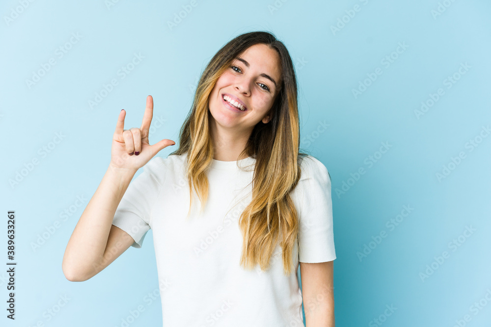 Fototapeta premium Young caucasian woman isolated on blue background showing a horns gesture as a revolution concept.