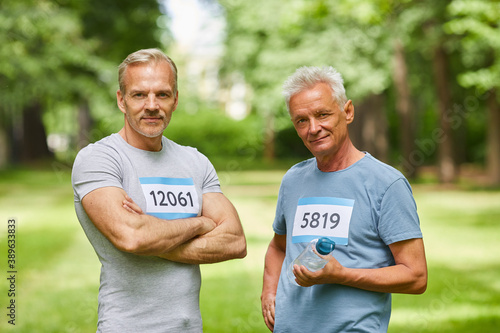 Medium portrait of two good-looking senior adult men, participants of summer marathon, standing together looking at camera