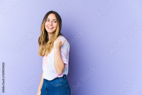Young caucasian woman isolated on purple background points with thumb finger away, laughing and carefree.
