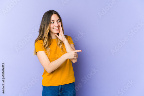 Young caucasian woman isolated on purple background saying a gossip  pointing to side reporting something.