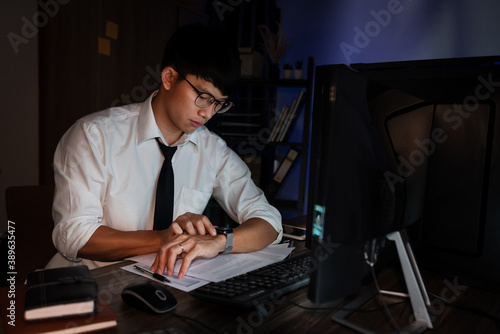 Asian businessman looking clock watch sitting at the desk working late, overtime night working or studying concept photo