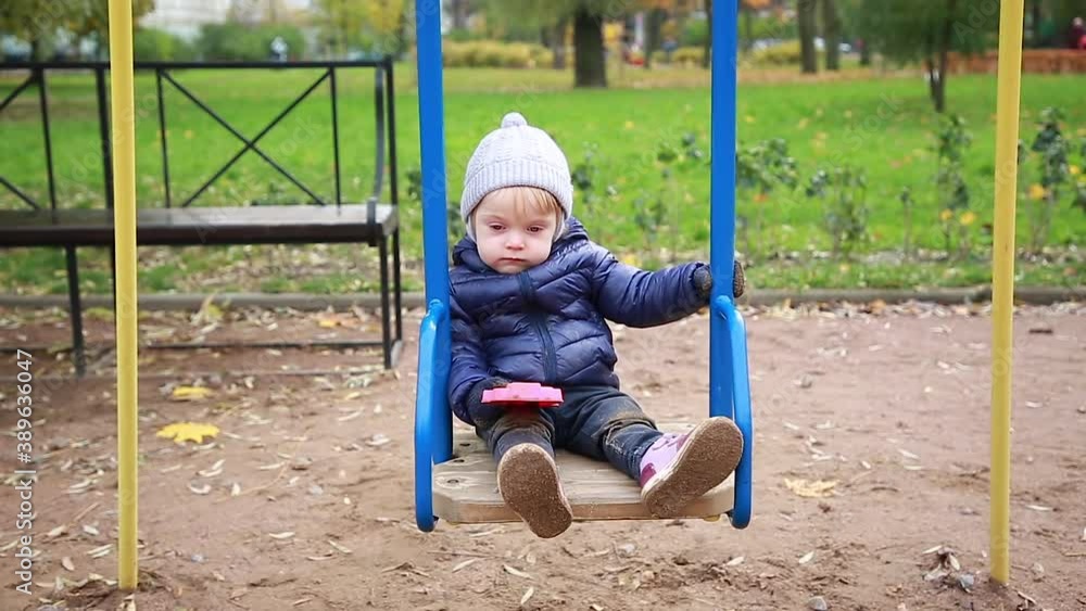 A small blond boy swings on a swing. Sad baby sitting on the ride, he wants to sleep. Playground. Childhood. A small blond boy swings on a swing. Sad baby sitting on the ride, he wants to sleep. Playground. Childhood.