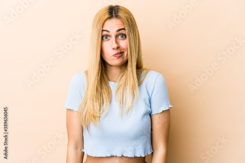 Young blonde caucasian woman shrugs shoulders and open eyes confused.