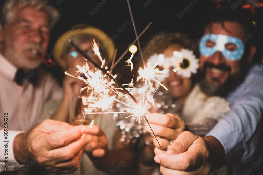 group of four people enjoying new year night celebrating with sparklers in the middle and looking at the camera - adults having fun together - obrazy, fototapety, plakaty 
