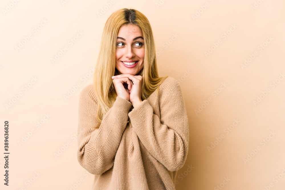 Young blonde caucasian woman keeps hands under chin, is looking happily aside. Young blonde caucasian woman keeps hands under chin, is looking happily aside.