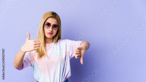 Young blonde caucasian woman showing thumbs up and thumbs down, difficult choose concept