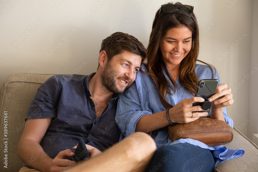 Young couple watching movie on cell phone and smiling on couch at living room Young couple watching movie on cell phone and smiling on couch at living room