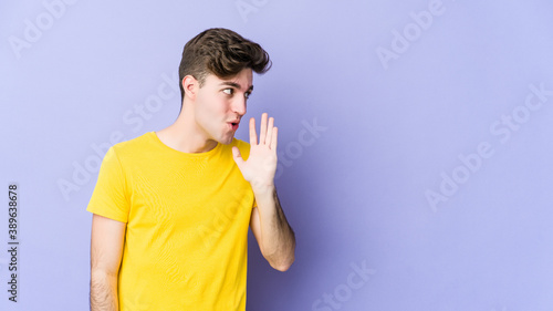 Young caucasian man isolated on purple background is saying a secret hot braking news and looking aside © Asier
