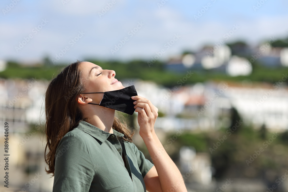 Woman taking off mask breathing fresh air in a town
