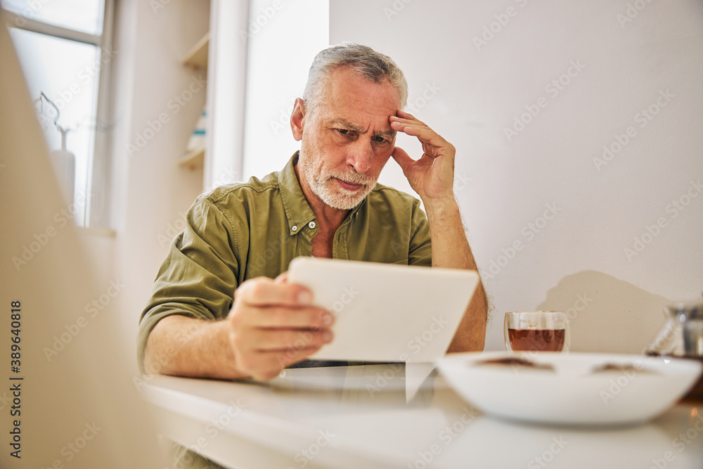 Serious elderly gentleman being concerned and looking at his tablet
