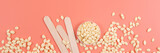 Wooden spatulas, depilation wax granules on pink background. Flat lay, beauty treatment concept. Banner for website