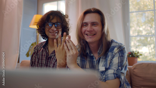 Happy gay couple getting marriage and showing ring to friend in front of laptop with video chat © TommyStockProject