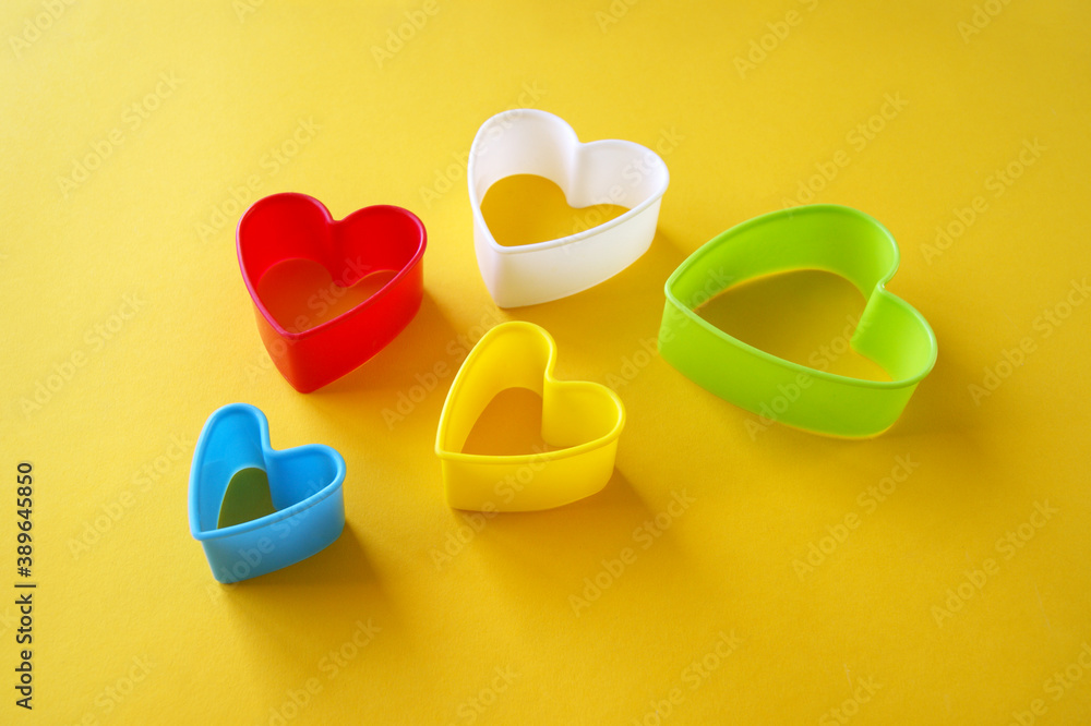 Naklejka premium Plastic molds of multi colors for making cookies in the shape of a hearts on a yellow background.