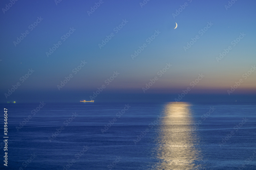 Schiff am Horizont nach Sonnenuntergang in der Nordsee mit der Mondsichel am Himmel