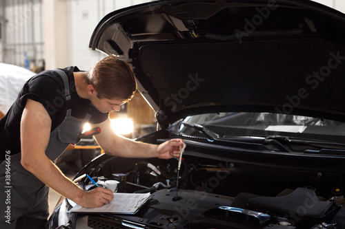 handsome caucasian guy is making notes while repairing hood of car, check all missing attributes inside of automobile © alfa27