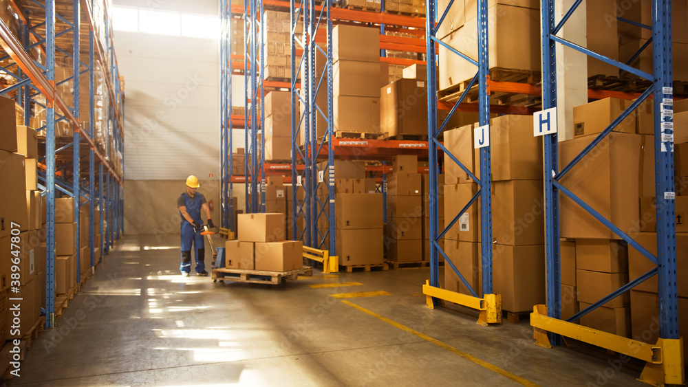 Worker Moves Cardboard Boxes using Manual Pallet Truck, Walking between Rows of Shelves with Goods in Retail Warehouse. People Work in Product Distribution Logistics Center. Side View Worker Moves Cardboard Boxes using Manual Pallet Truck, Walking between Rows of Shelves with Goods in Retail Warehouse. People Work in Product Distribution Logistics Center. Side View