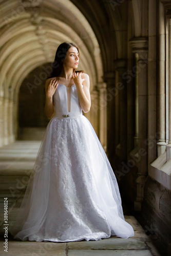 Beautiful girl wearing white wedding dress posing alone at a castle hall