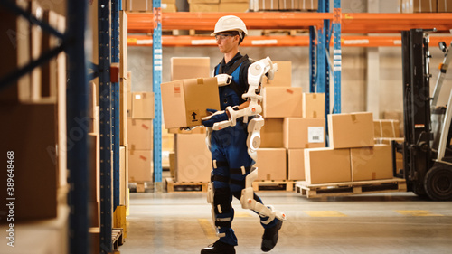High-Tech Futuristic Warehouse: Worker Wearing Advanced Full Body Powered exoskeleton, Walks with Heavy Cardboard Box. Exosuit amplifies Human Performance, strength, Eliminates Work Related Injuries