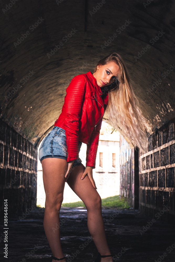 Naklejka premium Sexy girl posing with a red jacket and short jeans in a ruined building.