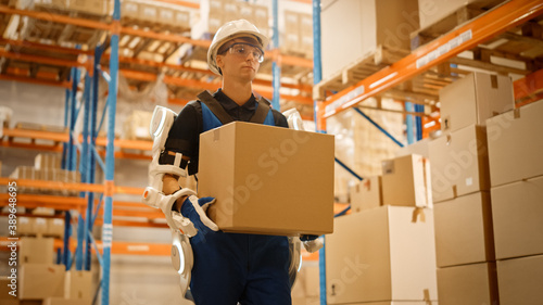 High-Tech Futuristic Warehouse: Worker Wearing Advanced Full Body Powered exoskeleton, Walks with Heavy Cardboard Box. Exosuit amplifies Human strength. Low Angle Portrait Shot