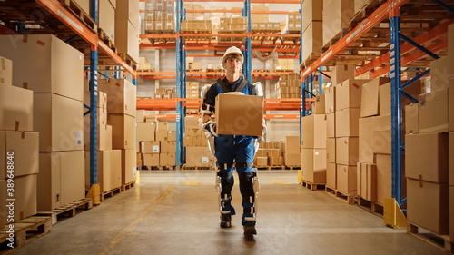 High-Tech Futuristic Warehouse: Worker Wearing Advanced Full Body Powered Exoskeleton, Walks with Heavy Cardboard Box. Package Delivery Exosuit amplifies Human strength. Portrait Shot