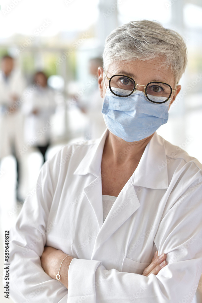 Portrait of mature woman doctor standing in hospital hallway with face mask on Portrait of mature woman doctor standing in hospital hallway with face mask on